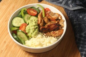 Chicken taco bowl recipe with spiced chicken, rice, avocado, and fresh salad vegetables in a family-style bowl meal.