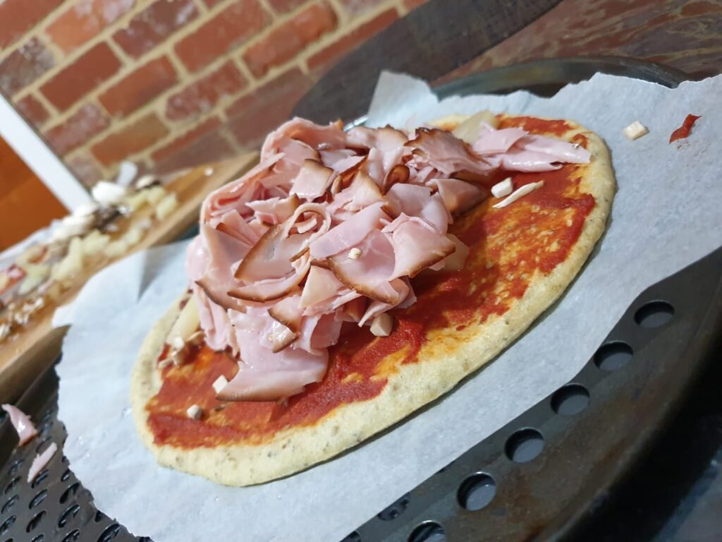 Pizza base with ham piled in the centre ready for a child to top during family pizza night at home
